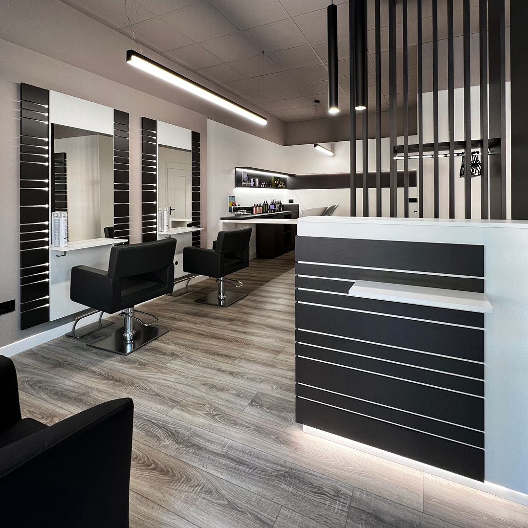 Immagine della reception con bancone bianco a strisce in legno nere e si intravedono tutte le poltrone dell'area stilistica